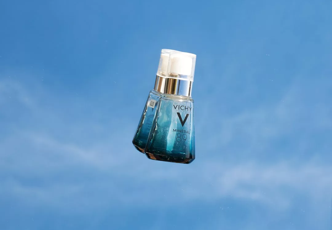 A bottle of Vichy Mineral 89 serum, embodying Glamesia elegance, is suspended in midair against a blue sky background.