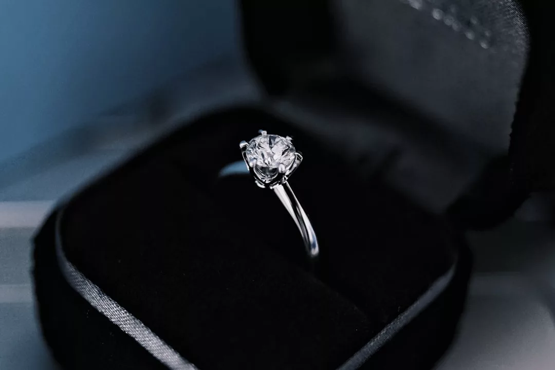 A silver ring with a single round diamond set in a prong setting is displayed in an open black velvet ring box, radiating Glamesia’s signature touch of fashion and luxury.