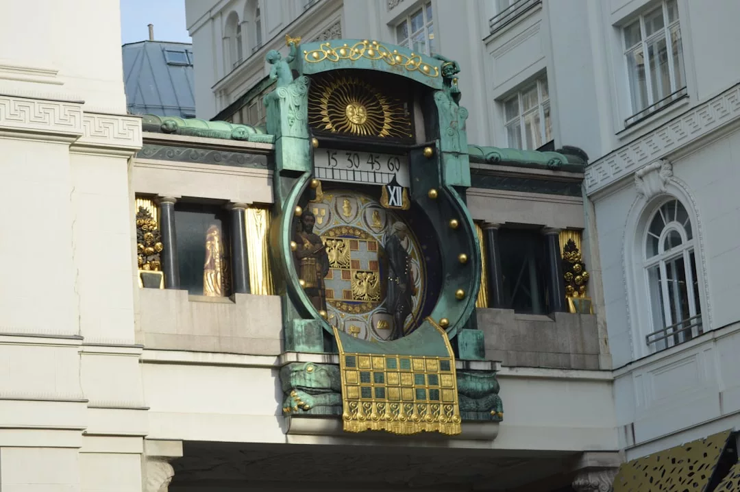 A decorative, historic clock with gold and green accents is mounted on a building facade, exuding luxury with its statues and large Roman numeral display.