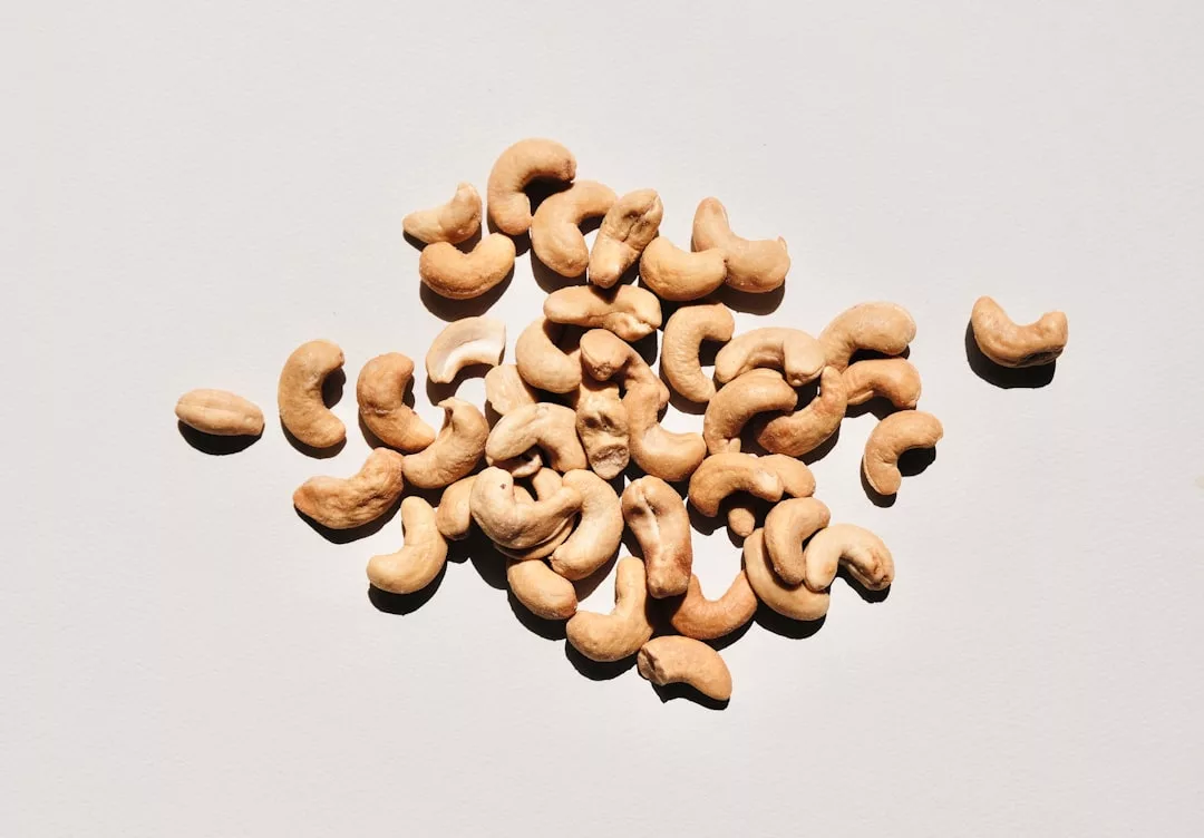 A pile of raw cashew nuts scattered on a plain white surface, adding a touch of natural luxury to your lifestyle.