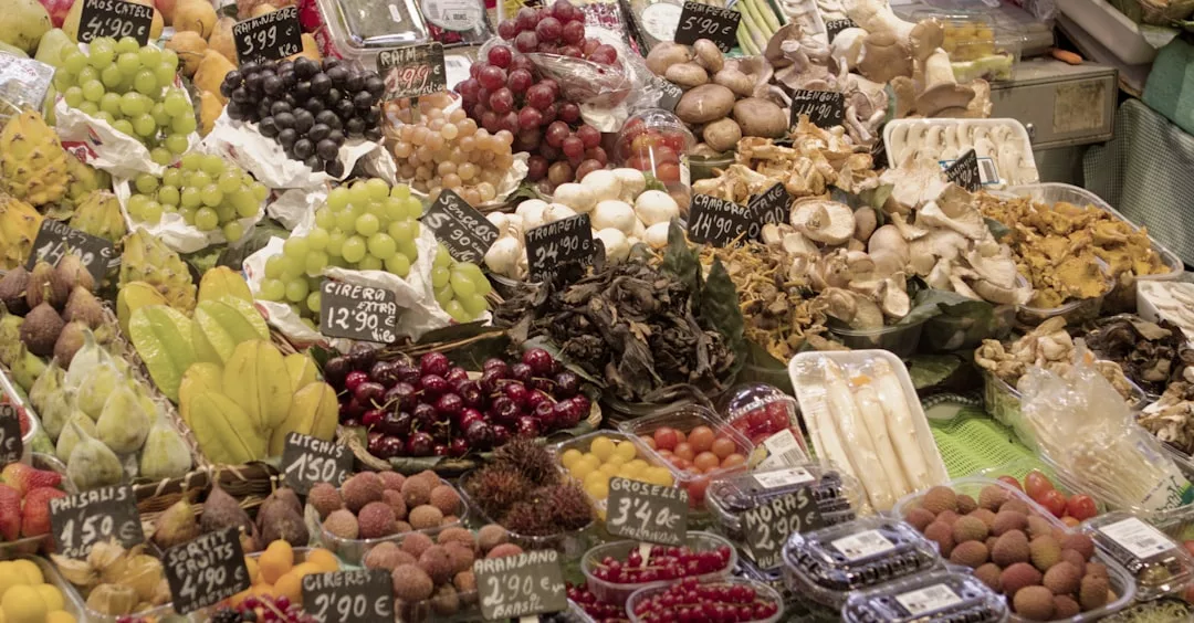 A market stall displays a variety of fresh fruits, mushrooms, and vegetables with handwritten price tags in euros, offering a taste of luxury for those who value a refined lifestyle.
