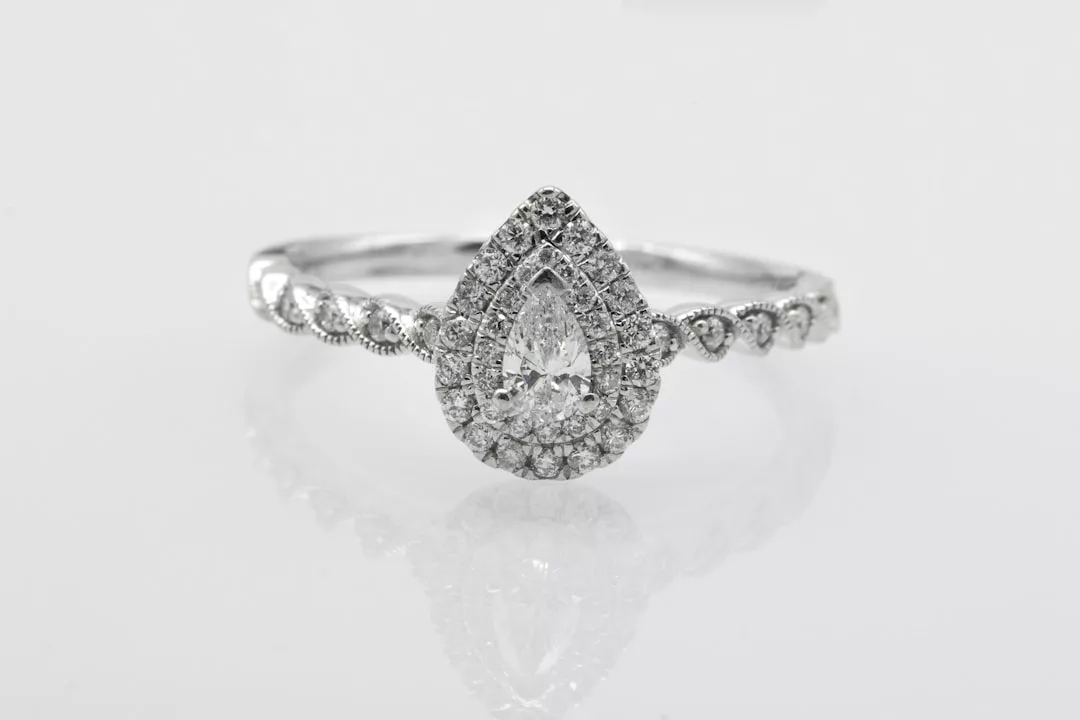 A silver ring with a pear-shaped center diamond, surrounded by smaller diamonds, and a band featuring additional round diamonds—perfect for adding a touch of luxury to your fashion and lifestyle.
