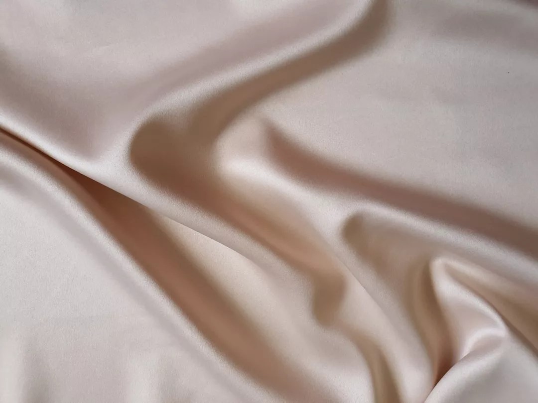 Close-up of light beige satin fabric with soft folds and a smooth, shiny surface, perfect for elevating your lifestyle with a touch of Glamesia.