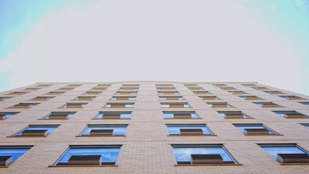 A low-angle view of a beige brick building with multiple rows of windows against a bright sky, capturing an architectural style that exudes Glamesia fashion and understated luxury.