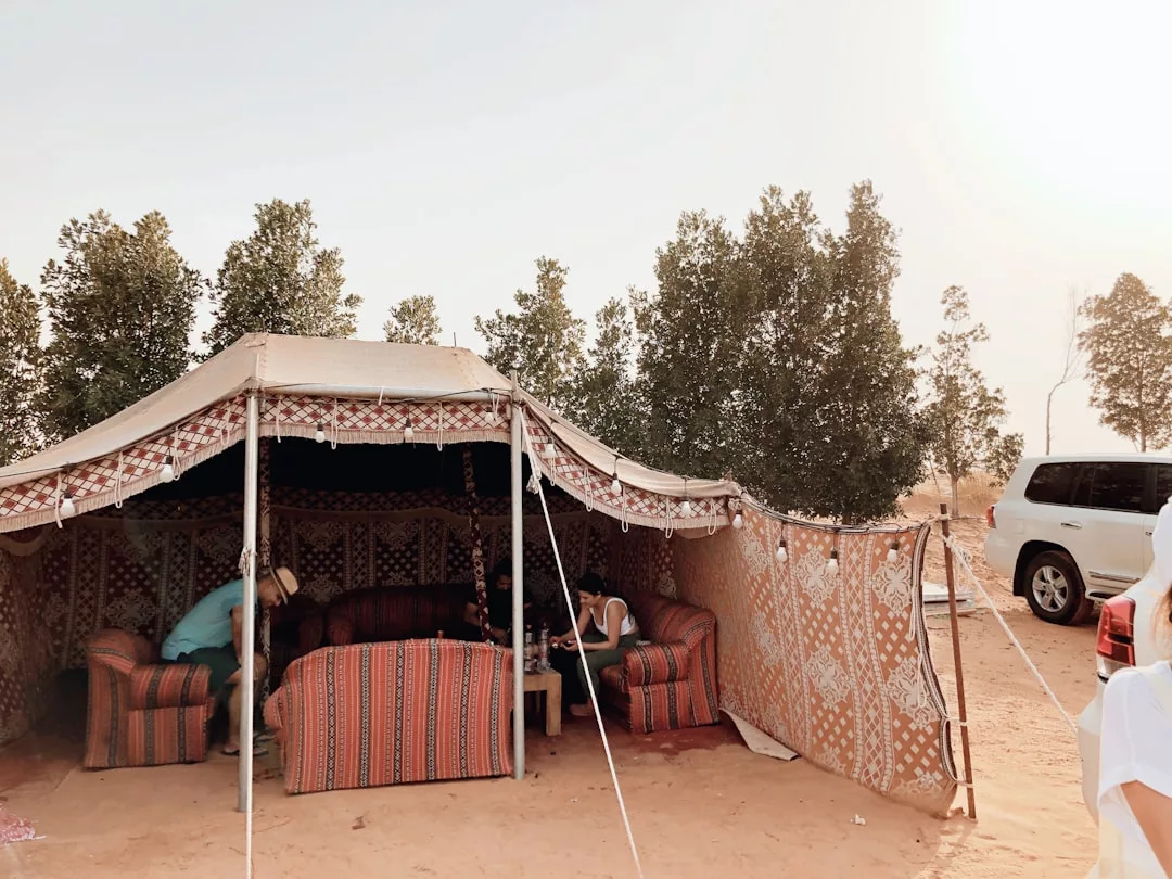 A traditional tent with patterned fabric walls and Laxary sofas set up in a sandy outdoor area, with trees and vehicles nearby.
