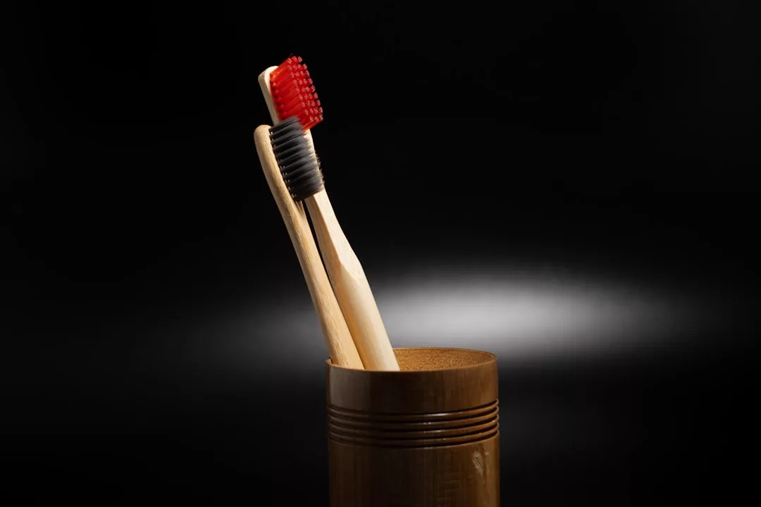 Two bamboo toothbrushes with red and black bristles stand upright in a wooden cup against a dark background, adding a touch of Laxary to your daily routine.