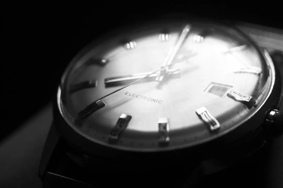 Close-up of an analog wristwatch displaying the word "ELECTRONIC" on its face, with metallic hour markers and hands, partially illuminated in low light—a perfect fusion of fashion and lifestyle elegance.