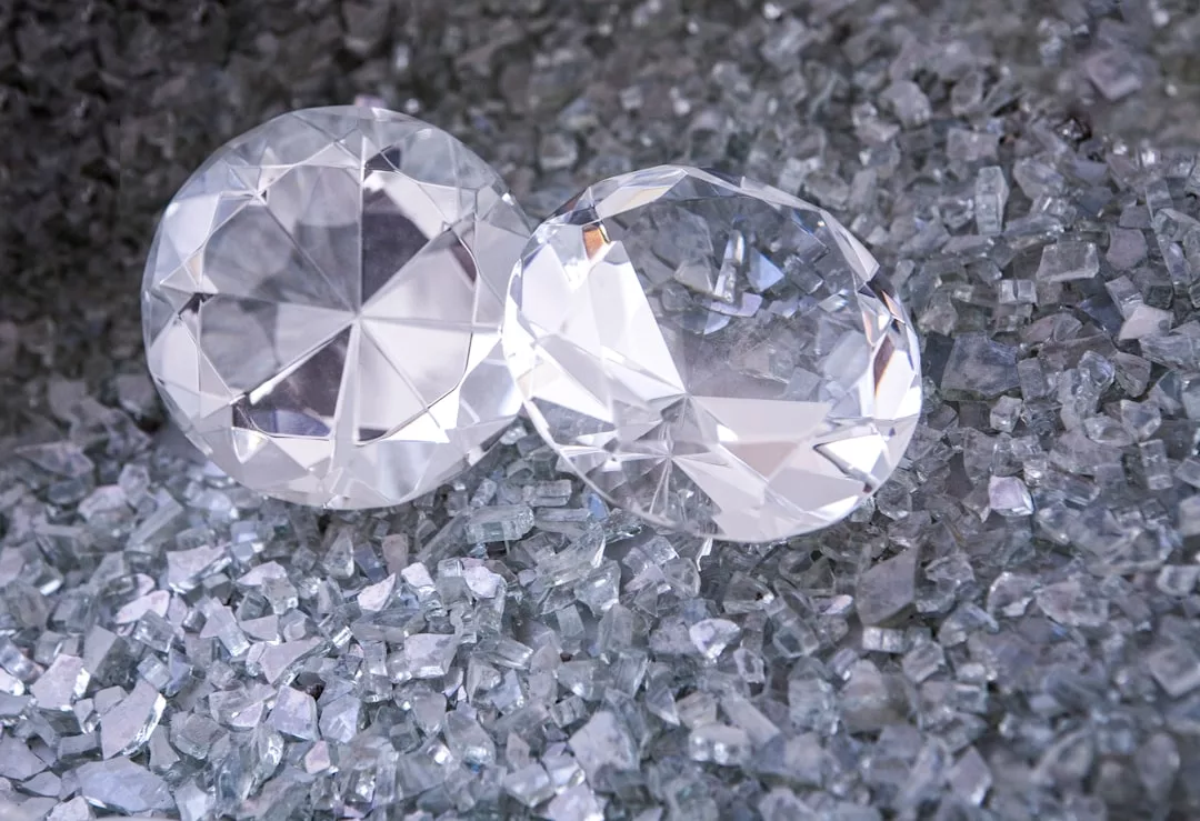 Two large, round-cut clear gemstones rest on a surface scattered with small, irregular crystal fragments, capturing the essence of luxury and sophisticated fashion.