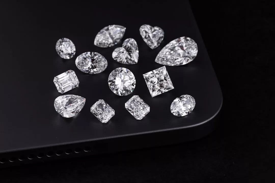 Various loose diamonds of different shapes and cuts are elegantly displayed on the corner of a black electronic device, possibly a laptop or tablet, adding a touch of luxury against the dark background.