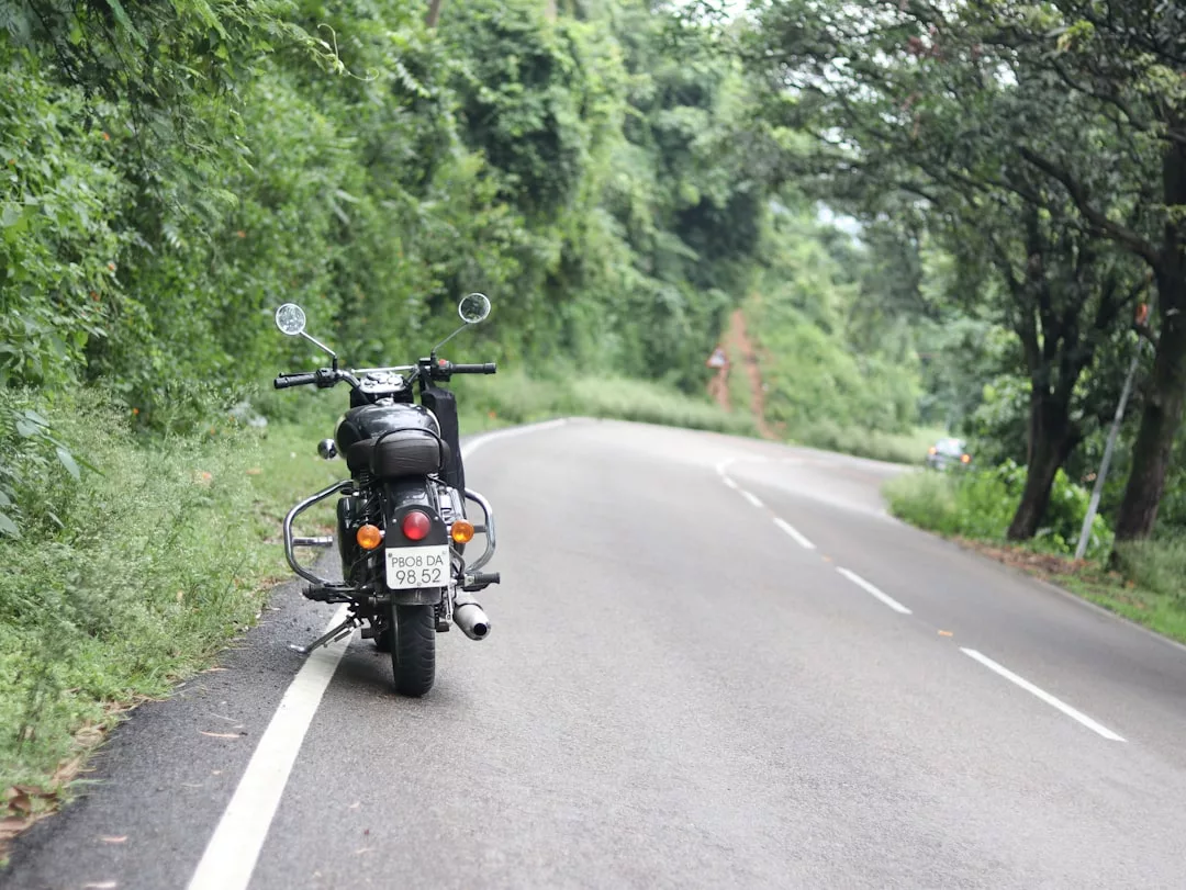 A black luxury motorcycle is parked on the roadside next to a winding road bordered by dense green trees and foliage.