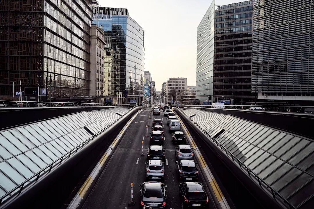 A city street with several lanes of cars in traffic, surrounded by tall modern office buildings and glass structures on both sides, sets the backdrop for a luxury lifestyle in the heart of Glamesia.