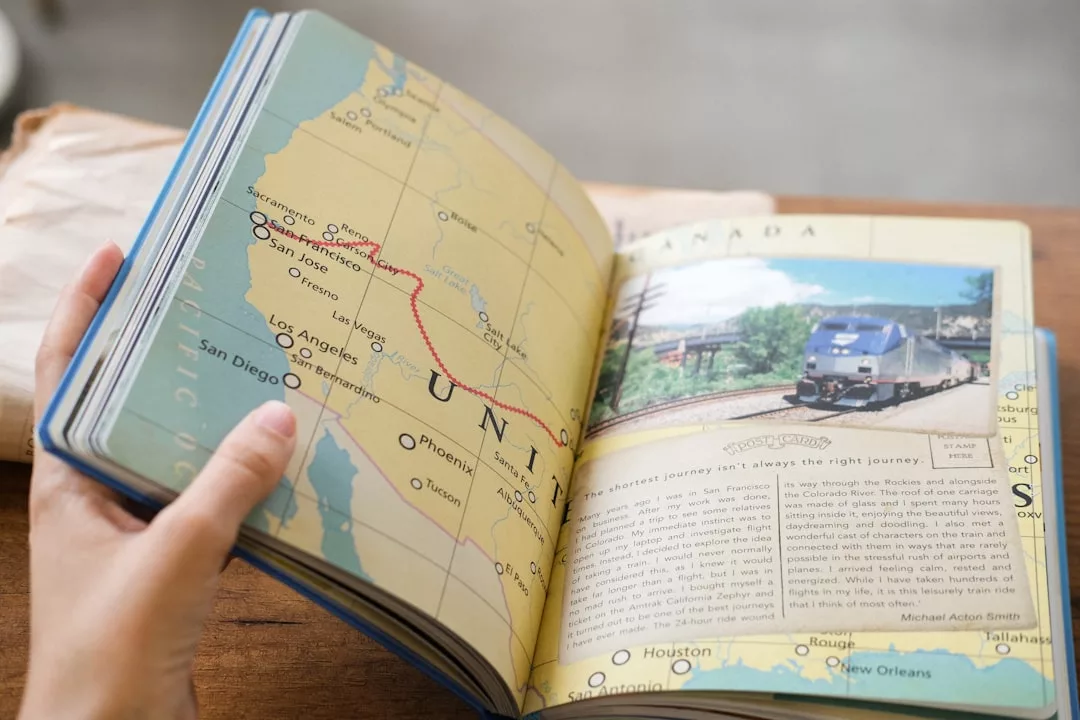 A person holds open a Glamesia book showing a map of the western United States with a luxury travel route and a page featuring a photo of a train and descriptive text.