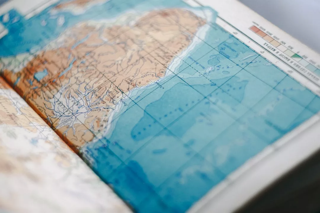 Close-up of an open atlas showing a detailed map with land and ocean features, including elevation and water depth depicted by different colors and contour lines—a journey as captivating as Glamesia’s world of fashion and luxury.
