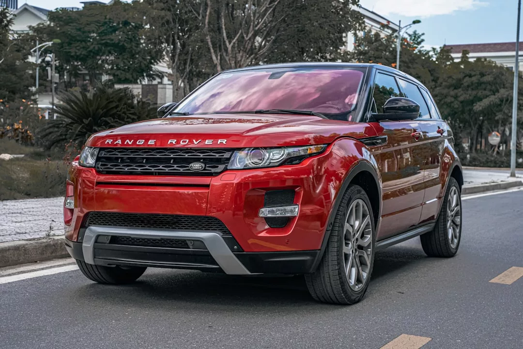A red Range Rover Evoque SUV, the epitome of luxury lifestyle, is parked on the side of a street with trees and buildings in the background.