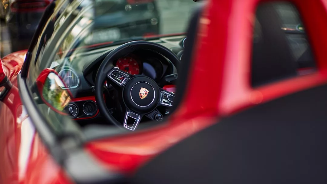 Close-up view of the interior of a red Porsche sports car, focusing on the steering wheel with the Porsche logo—perfectly capturing a luxe lifestyle and Glamesia-inspired fashion statement.