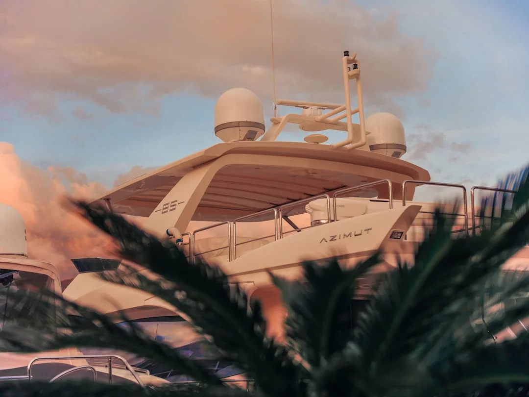 A luxury Azimut yacht is docked, partially obscured by palm leaves, with a cloudy sunset sky in the background—a true symbol of refined lifestyle.