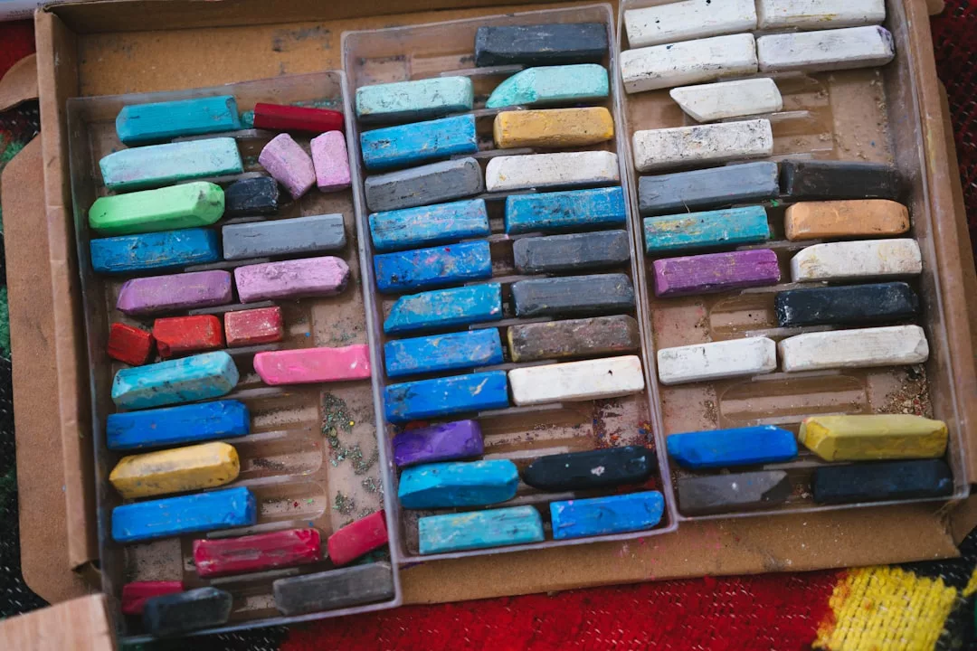 A cardboard box containing assorted colorful pastel sticks arranged in three plastic trays, showing signs of use—perfect for adding a touch of artistic flair to your creative lifestyle.