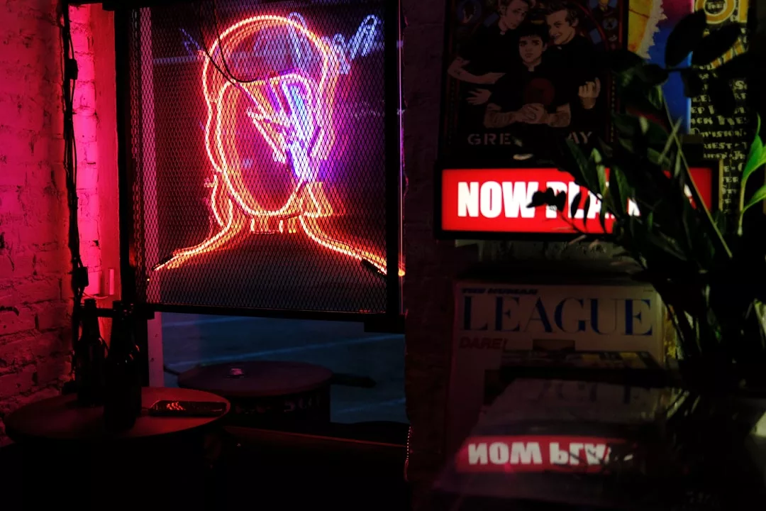 A neon outline of a head with a lightning bolt glows on a metal mesh wall in a dimly lit room, surrounded by posters and a "NOW" sign—creating an edgy yet luxury lifestyle vibe.