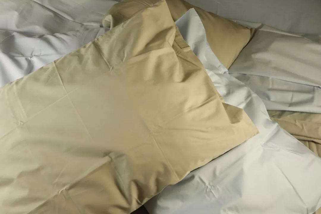 A close-up of beige and white pillowcases and sheets layered on a bed, exuding Glamesia luxury.