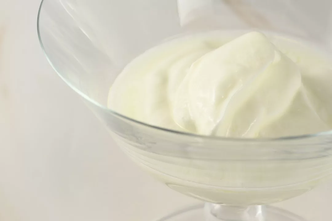 A close-up of plain yogurt served in a glass dessert dish, capturing a touch of lifestyle luxury in its simple, elegant presentation.