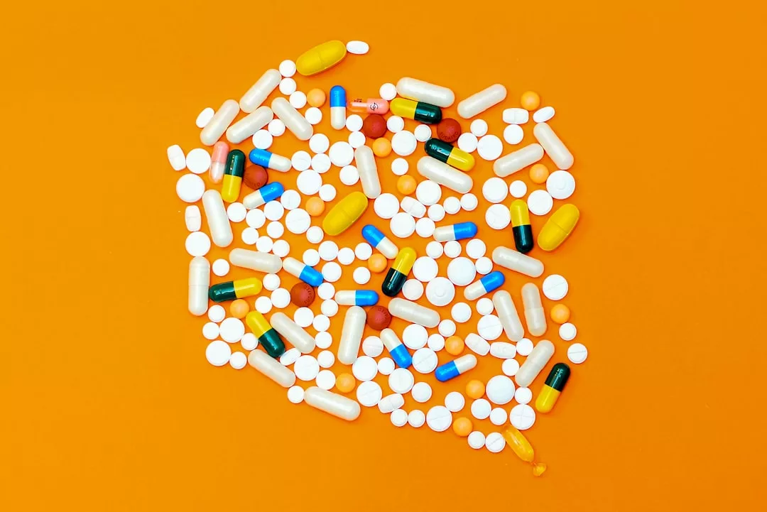 A variety of pills and capsules in different shapes, sizes, and colors scattered on an orange background, reflecting a modern lifestyle.