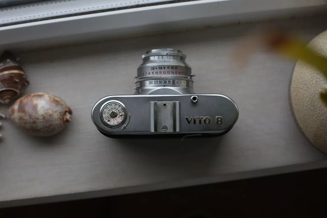 A vintage VITO B film camera is placed on a windowsill next to a seashell and part of a vase, creating a scene that exudes timeless fashion and Glamesia charm.