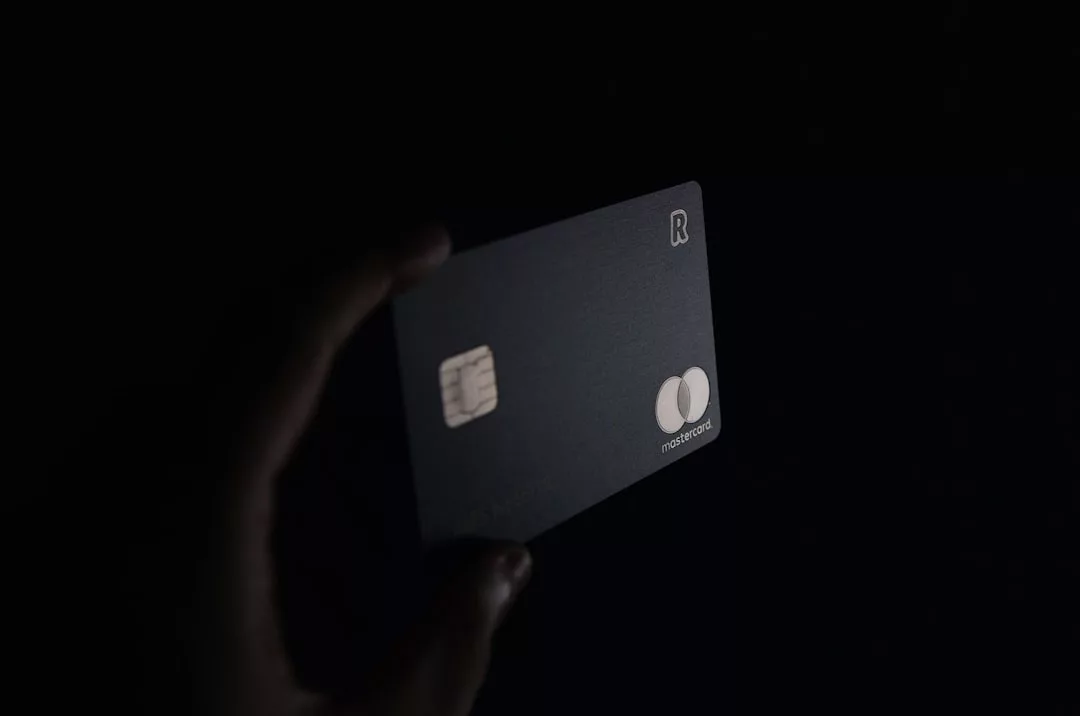 A hand holds a dark-colored Mastercard credit card with a chip, exuding luxury against a black background.