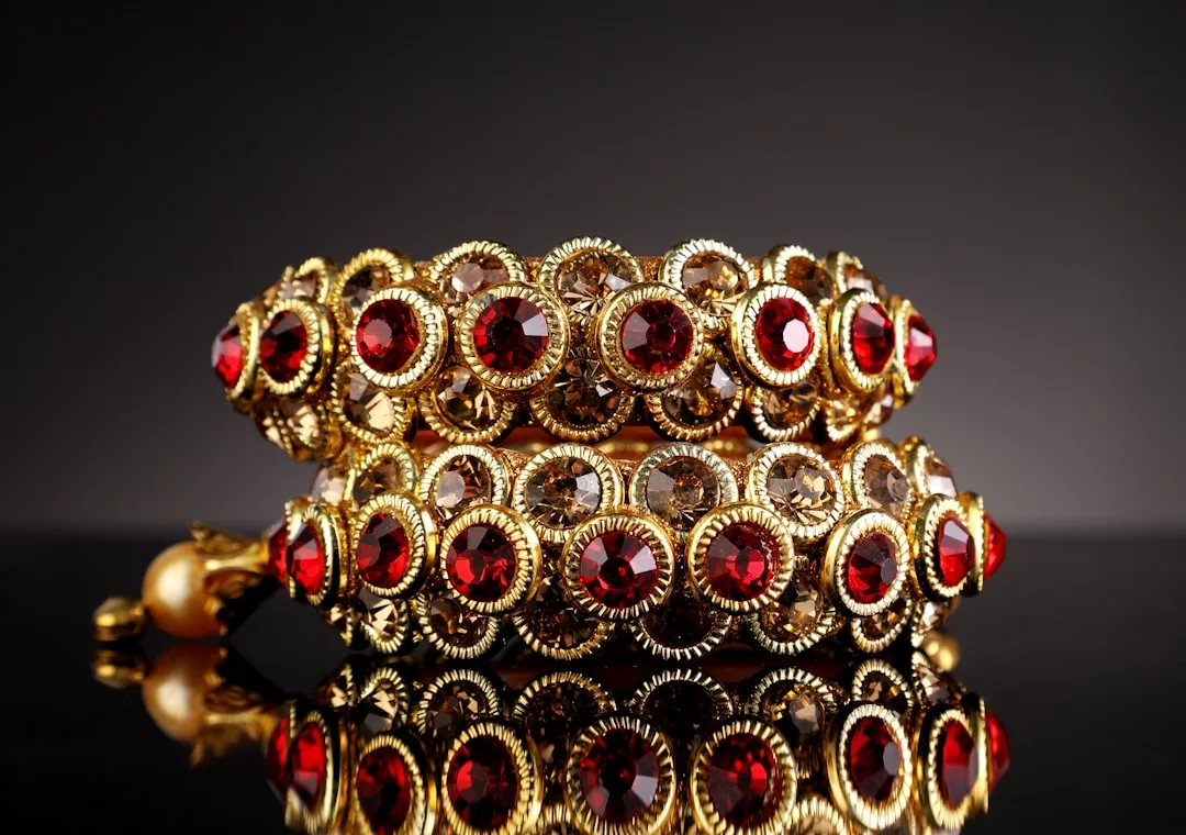 Two ornate gold bangles adorned with alternating red and clear gemstones are displayed against a dark background, capturing the essence of timeless fashion and luxury.