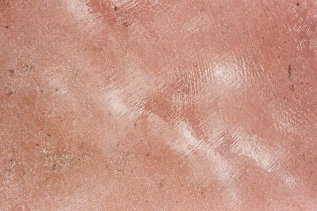 Wet textured surface with a reddish-brown color, showing subtle reflections and patterns created by water, evoking a sense of luxury and refined lifestyle.
