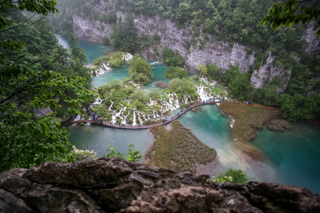 Elevated view of a winding wooden walkway over turquoise lakes and small waterfalls, surrounded by lush green trees and rocky cliffs—a true luxury escape for those with a passion for travel and an eye for lifestyle inspiration.