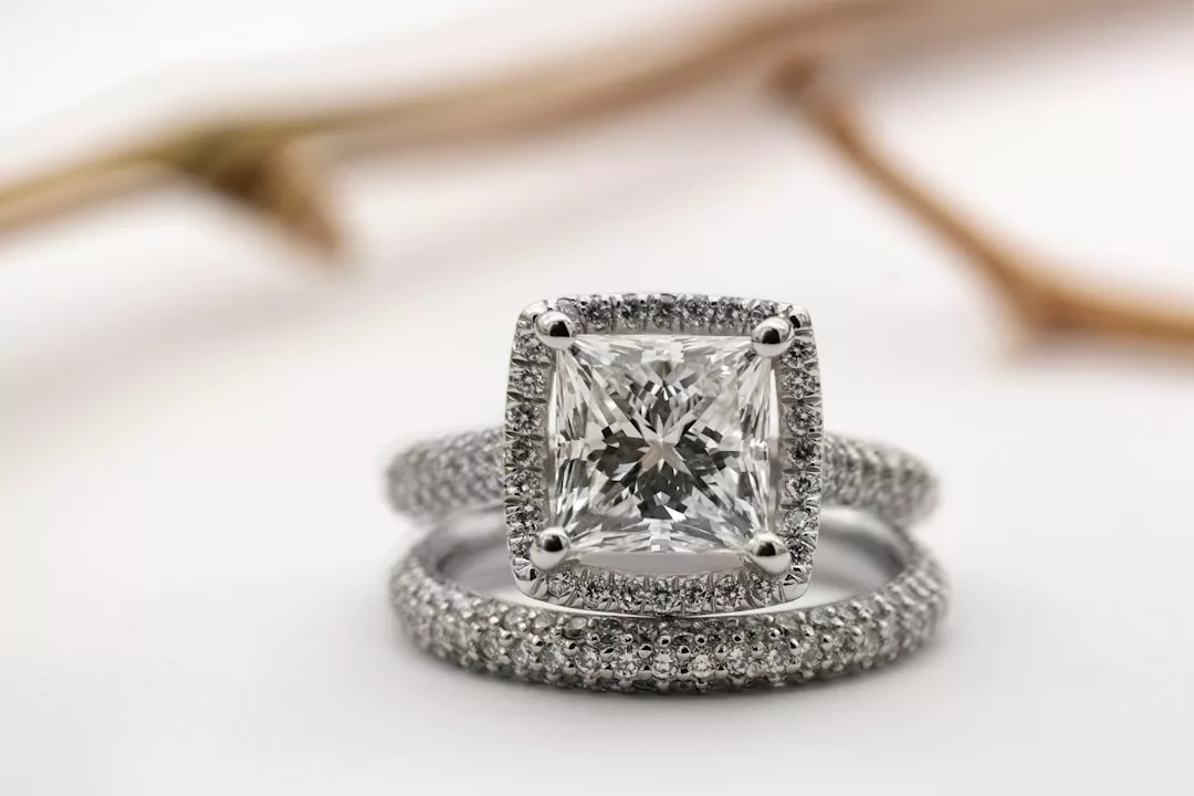 A close-up of a luxury cushion-cut diamond engagement ring and a matching diamond-studded wedding band, both set in white metal.
