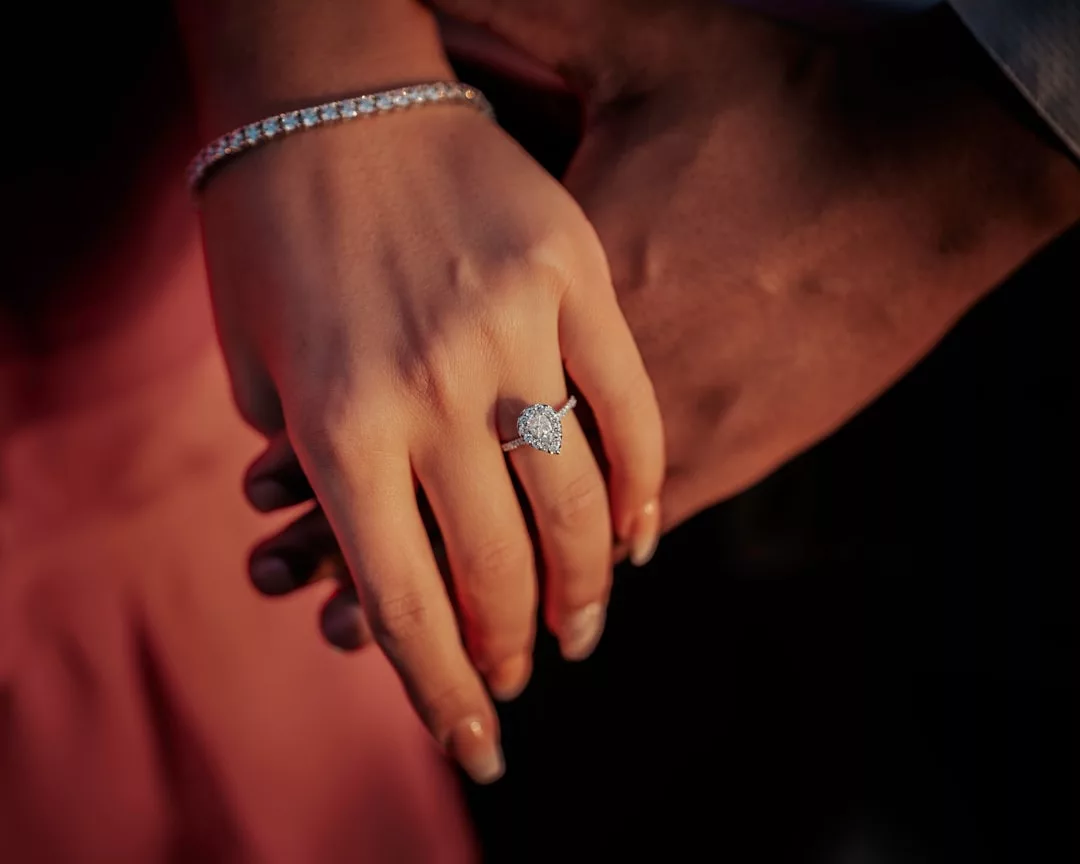 A close-up of a hand wearing a Laxary diamond ring and bracelet, gently held by another hand in the background.