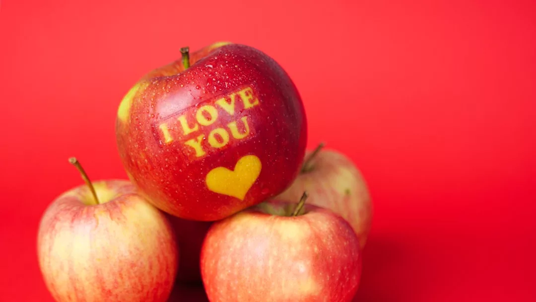 Four apples on a red background, the top apple featuring "I LOVE YOU" and a heart symbol etched onto its skin—a touch of luxury and style for lovers of unique fashion statements.