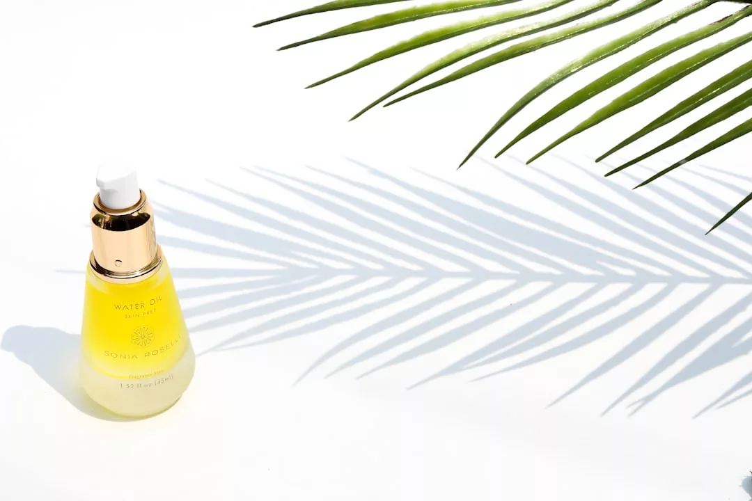 A yellow bottle of facial oil with a gold cap sits on a white surface, next to the shadow of a palm leaf, capturing an essence of luxury and effortless lifestyle.