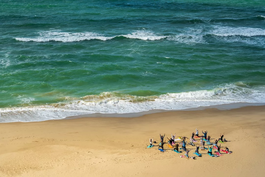 A group of people practice yoga on a sandy beach near the shoreline, embracing a serene lifestyle with green ocean waves in the background.