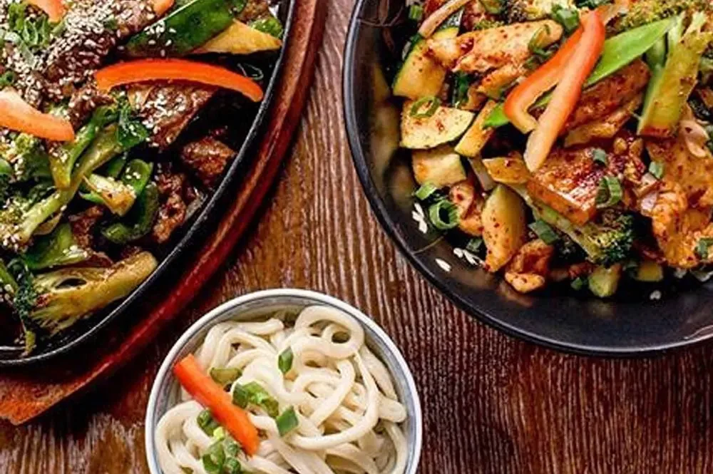 Two wok dishes and a noodle bowl seen from above